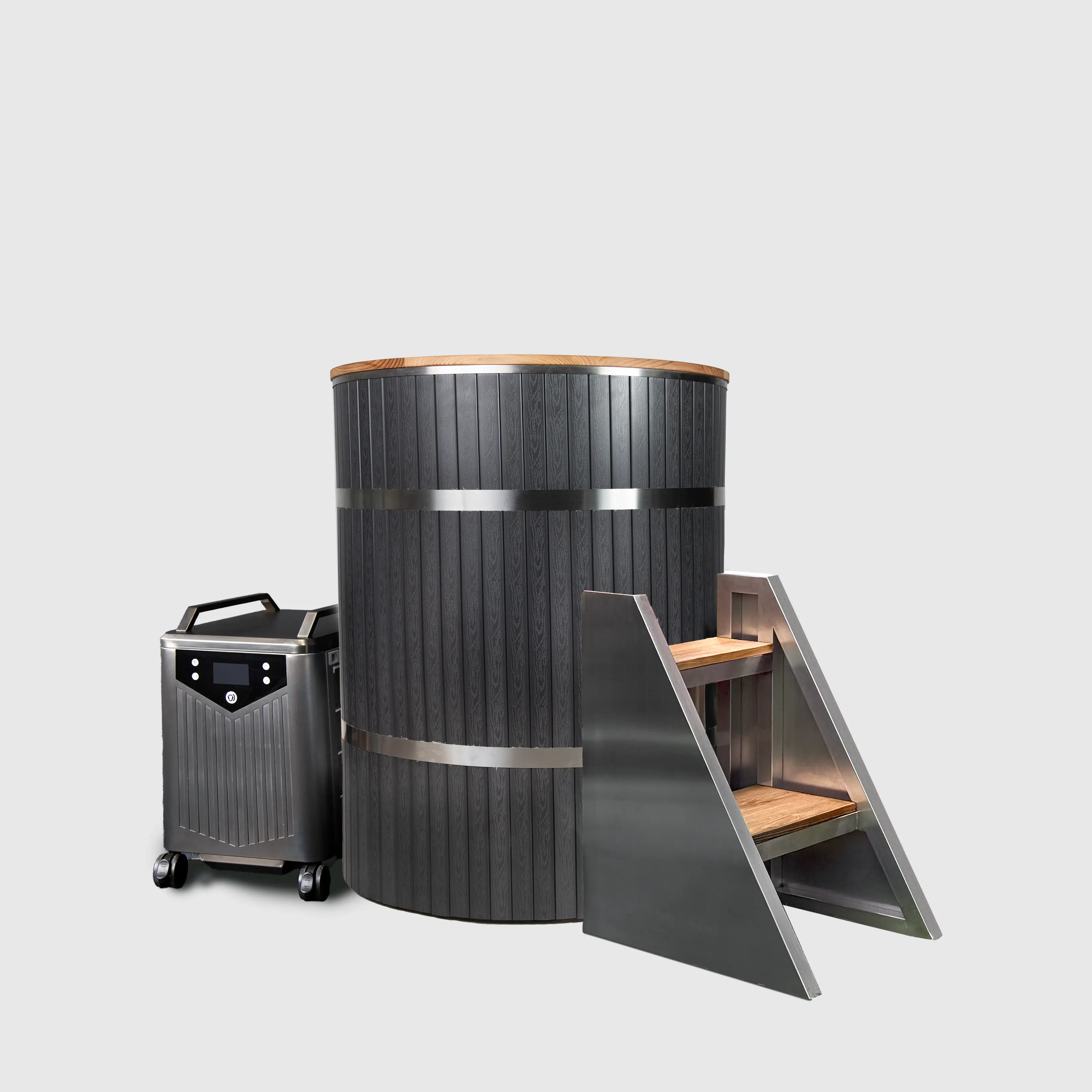 The Star Treatment 2.0 Cold Plunge features a tall, black cylindrical wooden tub with metal bands, a premium cooling unit on wheels, and a set of three metal and wood steps on the right, all set against a plain light gray background.