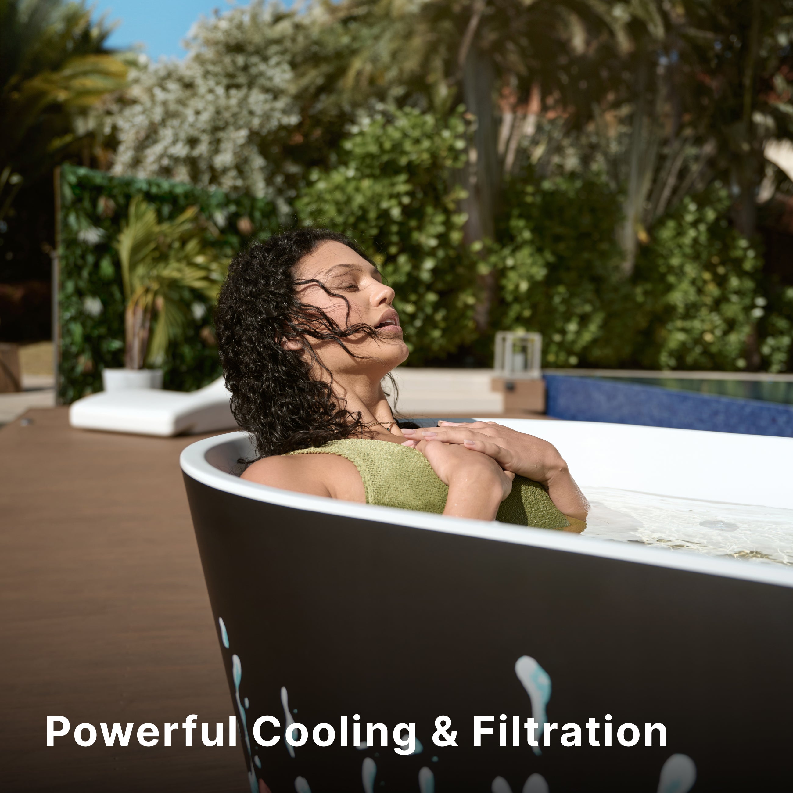A woman with curly hair relaxes in an outdoor tub, eyes closed and arms crossed over her chest. Lush greenery surrounds the scene. Text reads: “Powerful Cooling & Filtration.”.