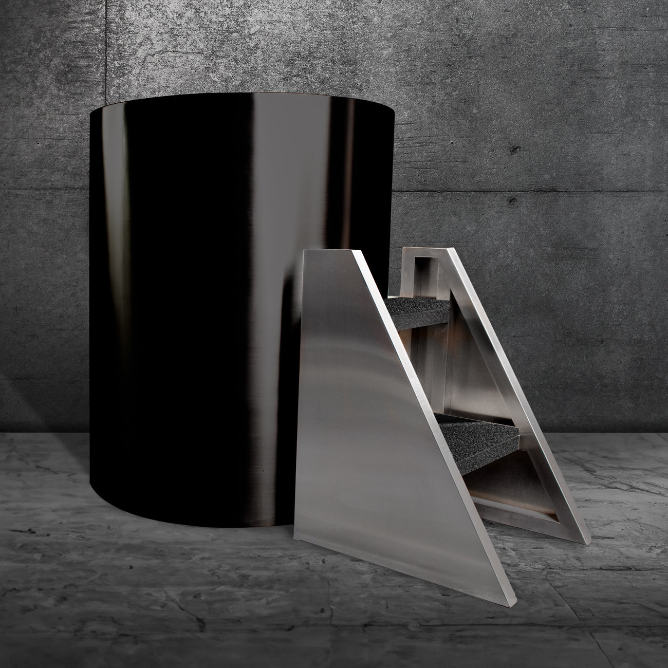 The Cyber Barrel Commercial, a sleek black cylindrical cold plunge made from marine-grade stainless steel for durability and optimal recovery, stands by a modern metal staircase with dark steps against textured gray concrete walls and floor.