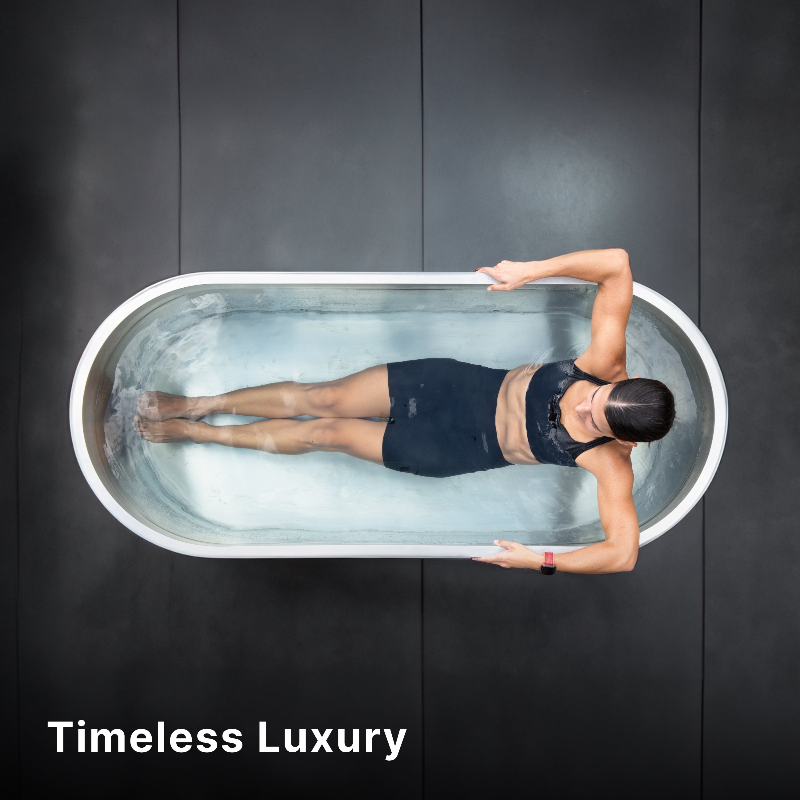 A woman in a black swimsuit relaxes in a modern oval bathtub filled with water, seen from above. The background is dark, and the words Timeless Luxury appear in the lower left corner.