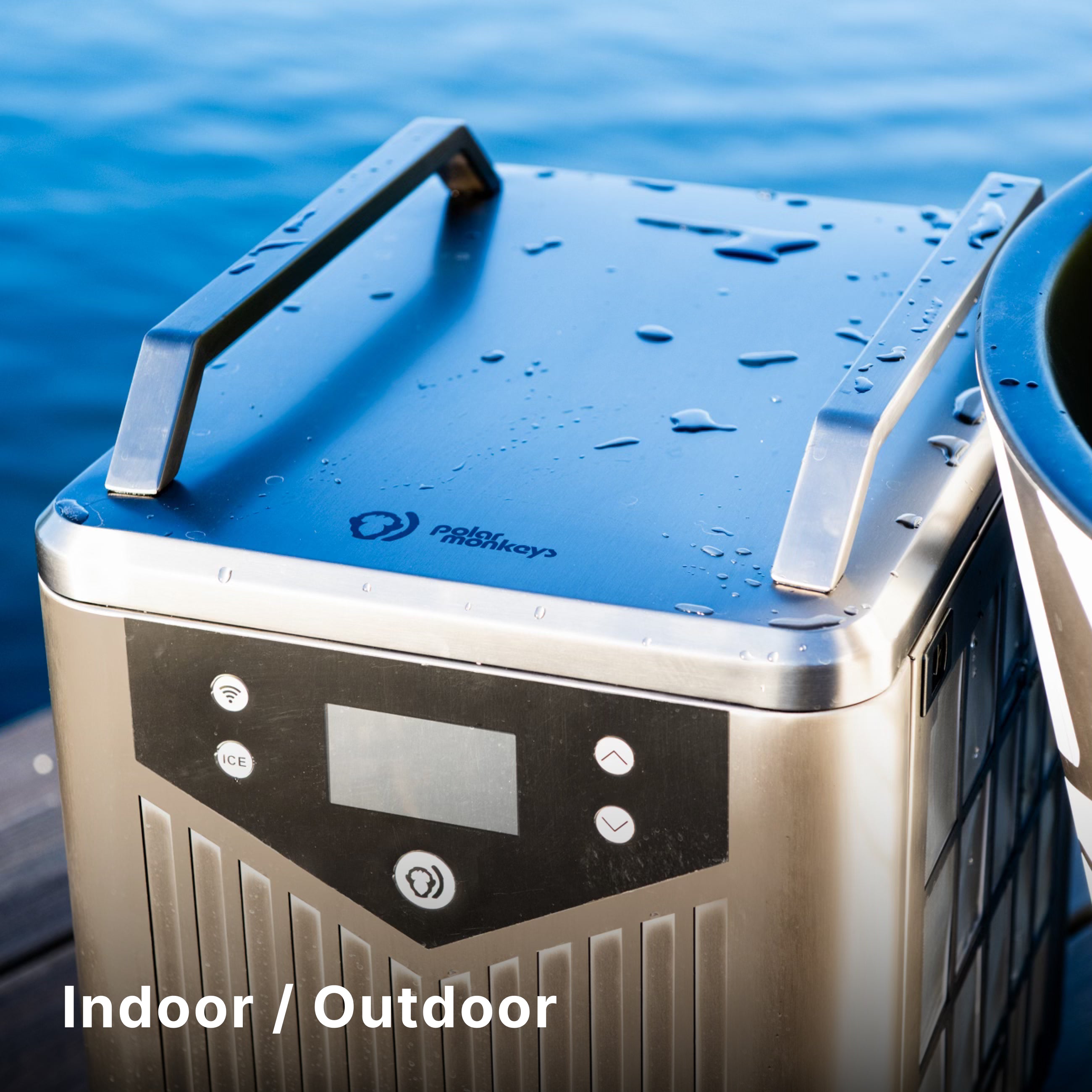 A modern stainless steel appliance with a digital display sits outdoors by the water, with droplets on its surface. The text Indoor / Outdoor appears in the lower left corner.