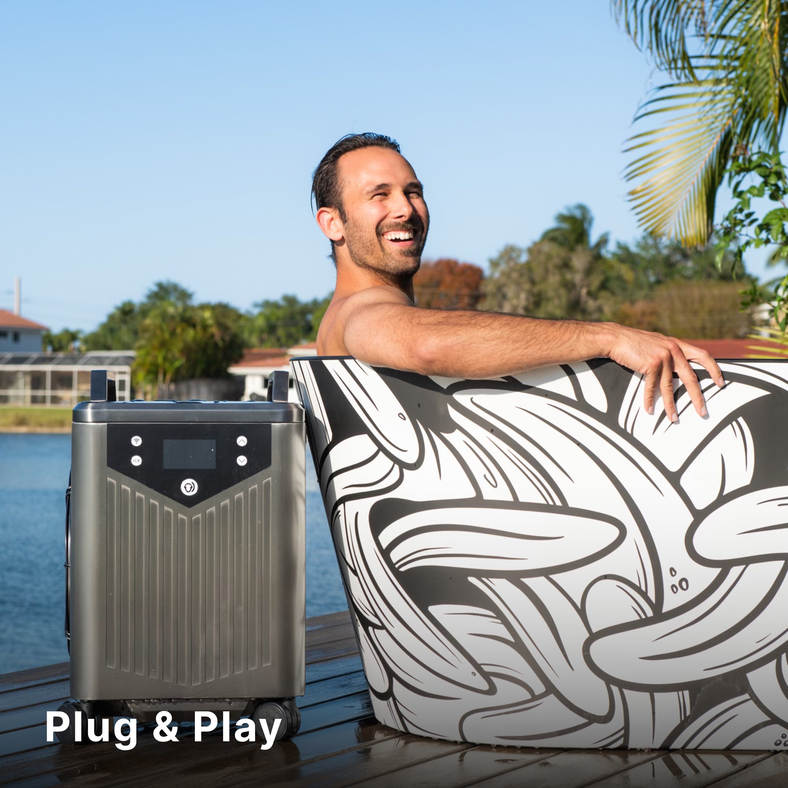 A smiling man sits in a patterned outdoor tub beside a sleek, gray plug-and-play device on a wooden deck, with palm trees, water, and houses in the background. The words Plug & Play appear in the lower left corner.
