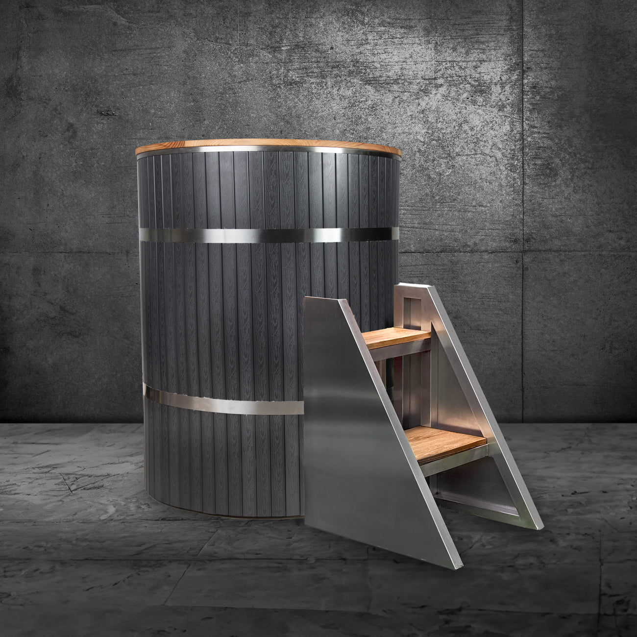 The Star Treatment 2.0 Commercial is a modern cylindrical cold plunge tub featuring a dark wood finish, stainless steel interior, metal bands, and matching steps of wood and metal, set against a textured concrete wall and floor.