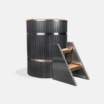 The Star Treatment 2.0 Commercial Cold Plunge is a tall, round black tub with stainless steel bands and wood accents, plus a matching two-step wood and metal staircase for easy access—ideal for cold therapy sessions. Shown on a plain white background.