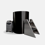 The Cyber Barrel Cold Plunge, a large black vertical cylindrical tank, stands beside a metal control box with a handle and control panel and metal stairs with black steps, all set against a plain white background.