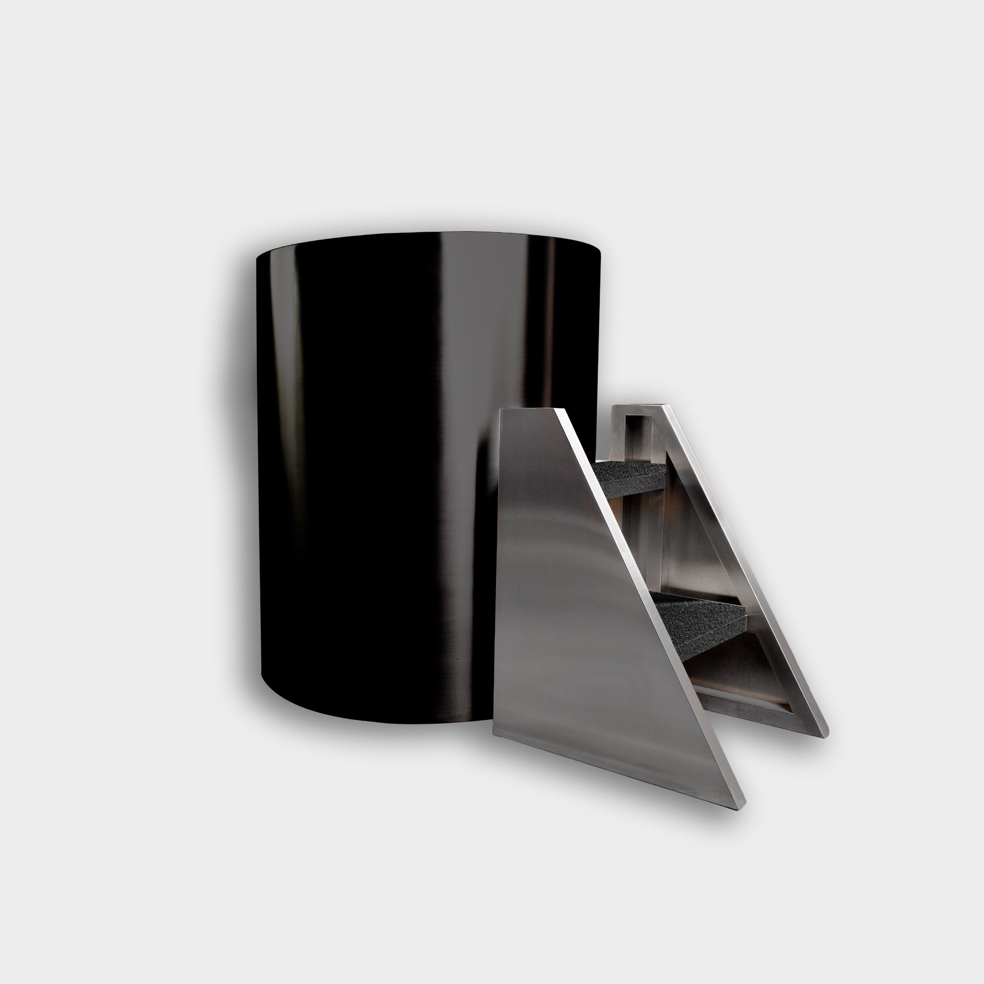 The Cyber Barrel Commercial Cold Plunge, featuring a glossy black vertical design, stands beside a modern metallic triangular staircase with two carpeted steps against a plain light gray background.
