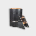 The Star Treatment 2.0 Commercial Cold Plunge is a tall, cylindrical wooden tub with metal bands for cold therapy, paired with angled wood and metal steps for easy access. Set against a plain, light gray background.
