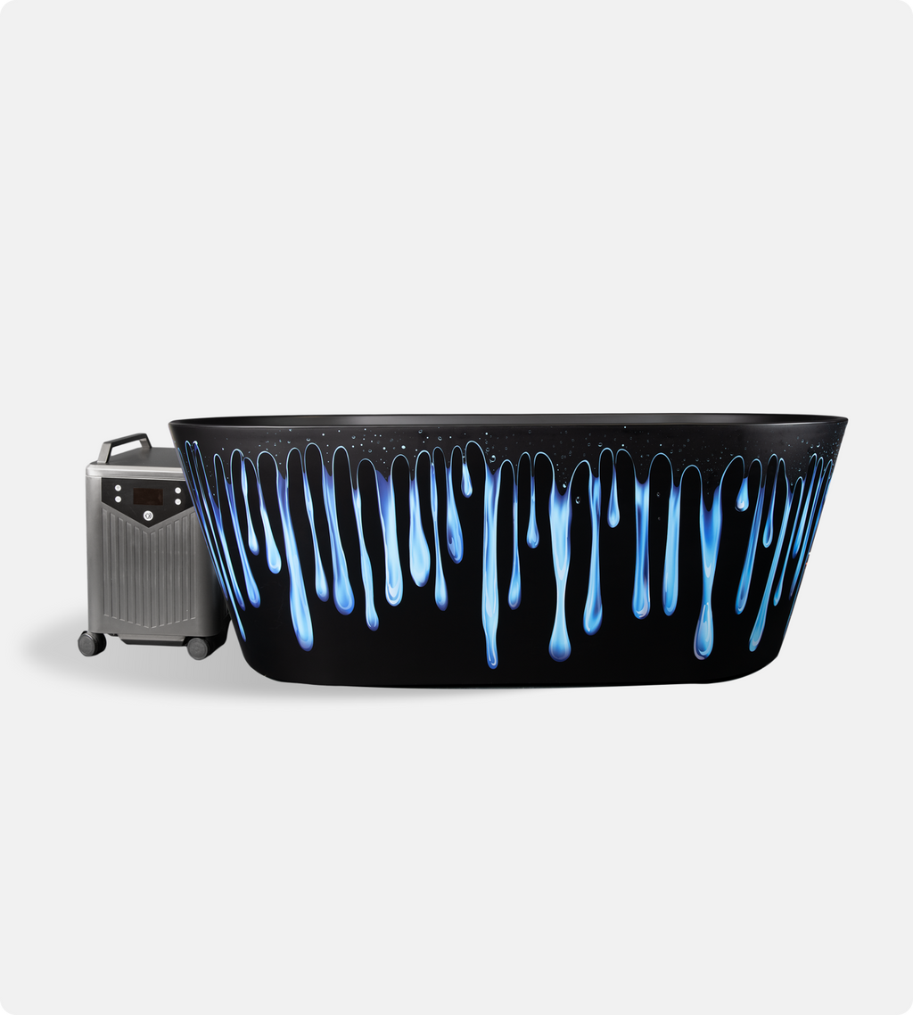 The Brainpod 2.0 Cold Plunge, a black artist-designed bathtub with blue and white paint drips, stands beside a gray portable device with control buttons and wheels on a plain white background.