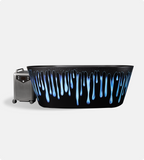 The Brainpod 2.0 Cold Plunge, a black artist-designed bathtub with blue and white paint drips, stands beside a gray portable device with control buttons and wheels on a plain white background.