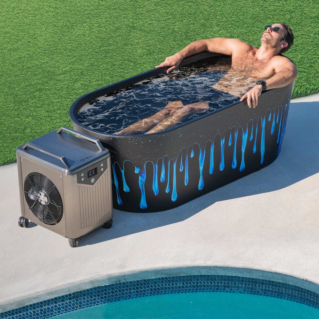 A man wearing sunglasses relaxes in a Brainpod 2.0 Cold Plunge tub with blue drips, filled with water, beside a pool. A cooling fan is set up next to the tub on the pool deck.