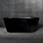 The Brainpod 2.0, a matte black freestanding bathtub with ergonomic design, sits on a gray marble floor against a textured dark gray concrete wall, creating a modern minimalist bathroom.