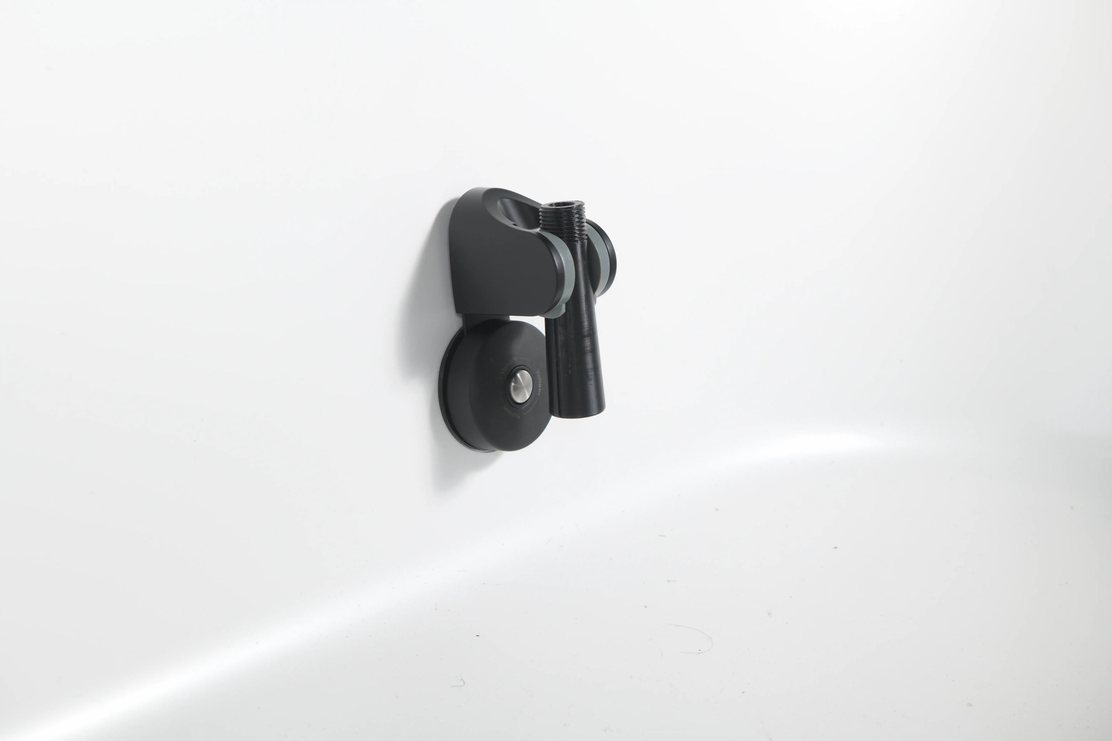 The Brainpod 2.0 Cold Plunge is a black, artist-designed wall-mounted holder with an ergonomic, cylindrical opening to securely hold your showerhead on a white bathroom wall.