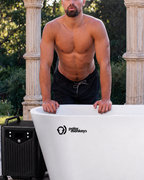 A shirtless man in black shorts stands by a white outdoor tub labeled “ONE by Polar Monkeys,” with a cooling chiller positioned beside the tub. Ancient-style columns and lush greenery in the background enhance the invigorating cold plunge experience.