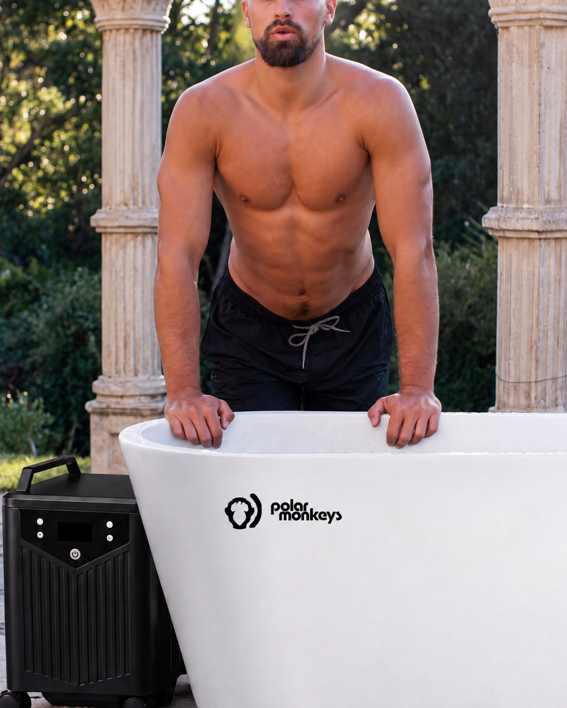 A shirtless man in black shorts stands by a white outdoor tub labeled “ONE by Polar Monkeys,” with a cooling chiller positioned beside the tub. Ancient-style columns and lush greenery in the background enhance the invigorating cold plunge experience.