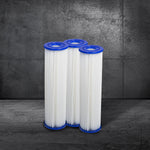 Three Polar Monkeys Filter Replacement for Residential Pro Systems cartridges (3 pack) with blue end caps stand upright on a gray surface, ready to power your cold plunge, against a dark concrete wall.