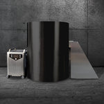 The Cyber Barrel, a sleek vertical cryotherapy chamber with a marine-grade stainless steel exterior, stands on a stone floor by a gray concrete wall beside its control unit and angled platform.