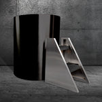 The Cyber Barrel Commercial, a sleek black cylindrical cold plunge made from marine-grade stainless steel for durability and optimal recovery, stands by a modern metal staircase with dark steps against textured gray concrete walls and floor.