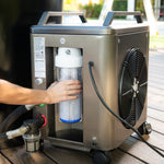 Someone is installing or removing a cylindrical filter from the ChillX Chiller, a portable stainless steel water filtration unit on wheels with a large fan and visible power cord for rapid cooling during your cold plunge outdoors.