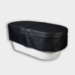 An Insulated Cold Plunge Cover in black, crafted from marine-grade synthetic leather with a zipper and fitted design, covers a white oval tub set against a plain light gray background.