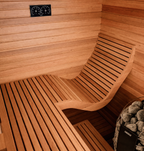 The Baia Glass Sauna features a modern wooden interior with a curved bench, temperature and humidity gauges mounted on the wall, and a Harvia-brand sauna heater with stones situated in the corner. An elegant glass sauna door enhances the sleek space, creating an open and inviting atmosphere.