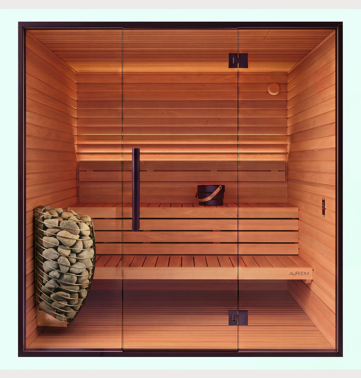The Mira Natural Sauna features modern wooden design with glass doors, a built-in bench, a bucket and ladle set placed on the bench, and sauna stones heating on the left side. This sauna offers a clean, tidy, and warmly lit natural atmosphere—perfect for relaxation.