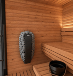 The Mira Natural Sauna is a modern indoor-outdoor sauna featuring wooden walls and benches, a black bucket and ladle placed on the lower bench, and a wall-mounted vertical electric heater filled with stones.