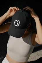 Someone in a light ribbed tank top adjusts their Polar Monkeys Cap, which is black with a white abstract logo and small brim text; the breathable hat mostly obscures their face.