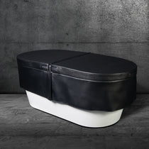 A white oval bathtub with an Insulated Cold Plunge Cover made from marine-grade synthetic leather sits on a gray marble floor against a textured concrete wall.