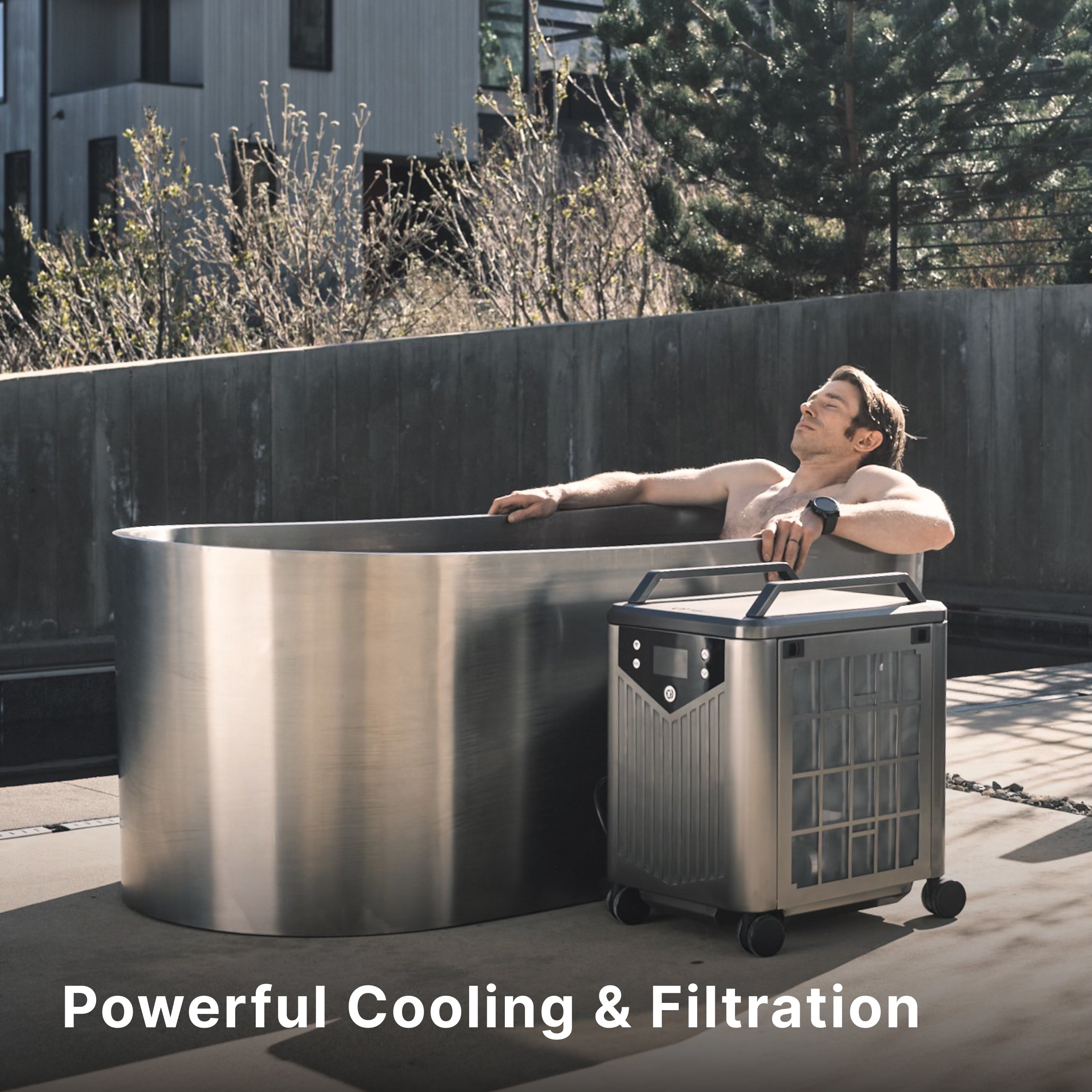 A man relaxes in a modern outdoor metal tub connected to a portable cooling and filtration unit on wheels. Text at the bottom reads, “Powerful Cooling & Filtration.”.