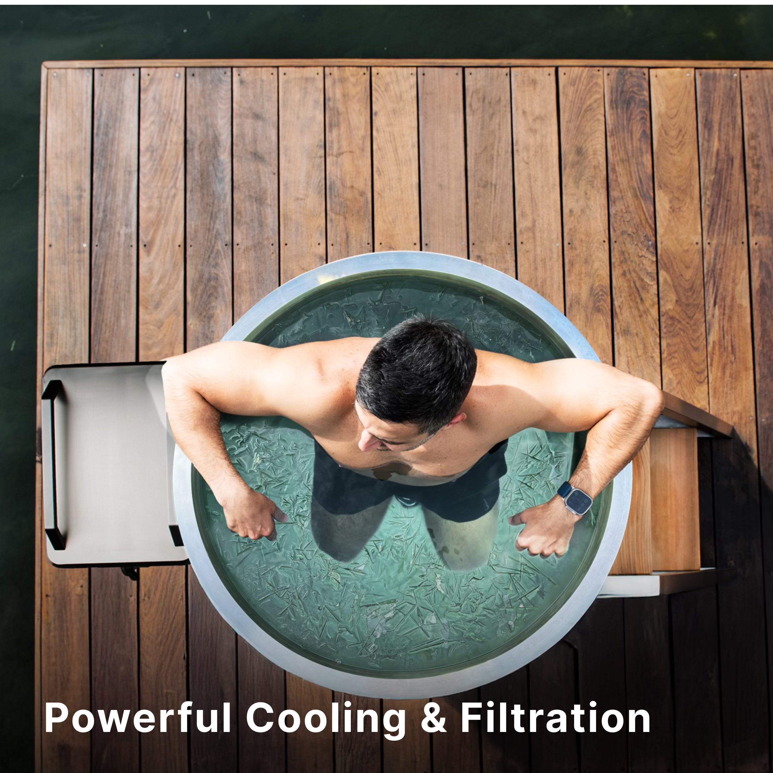 A man sits in a round ice bath on a wooden deck next to water, with ice floating in the tub. The text Powerful Cooling & Filtration appears at the bottom.