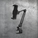 The PolarMonkeys Smart Device Holder, a black adjustable waterproof holder with a clamp base and flexible rotation arm, is mounted against a textured gray concrete wall.
