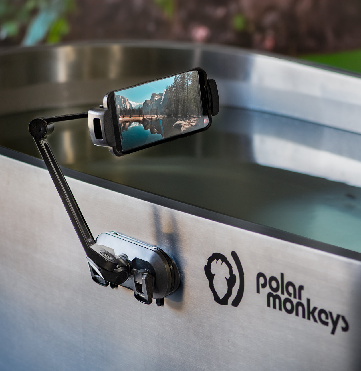 A smartphone is secured in the PolarMonkeys Smart Device Holder, a waterproof and flexible mount attached to a stainless steel ice bath, ideal for capturing scenic cold plunge moments.