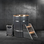 The Star Treatment 2.0 cold plunge tub, featuring wood paneling and metal bands, comes with a wheeled metal water chiller and a wooden step ladder for a sleek, compact setup—ideal against a dark concrete wall.