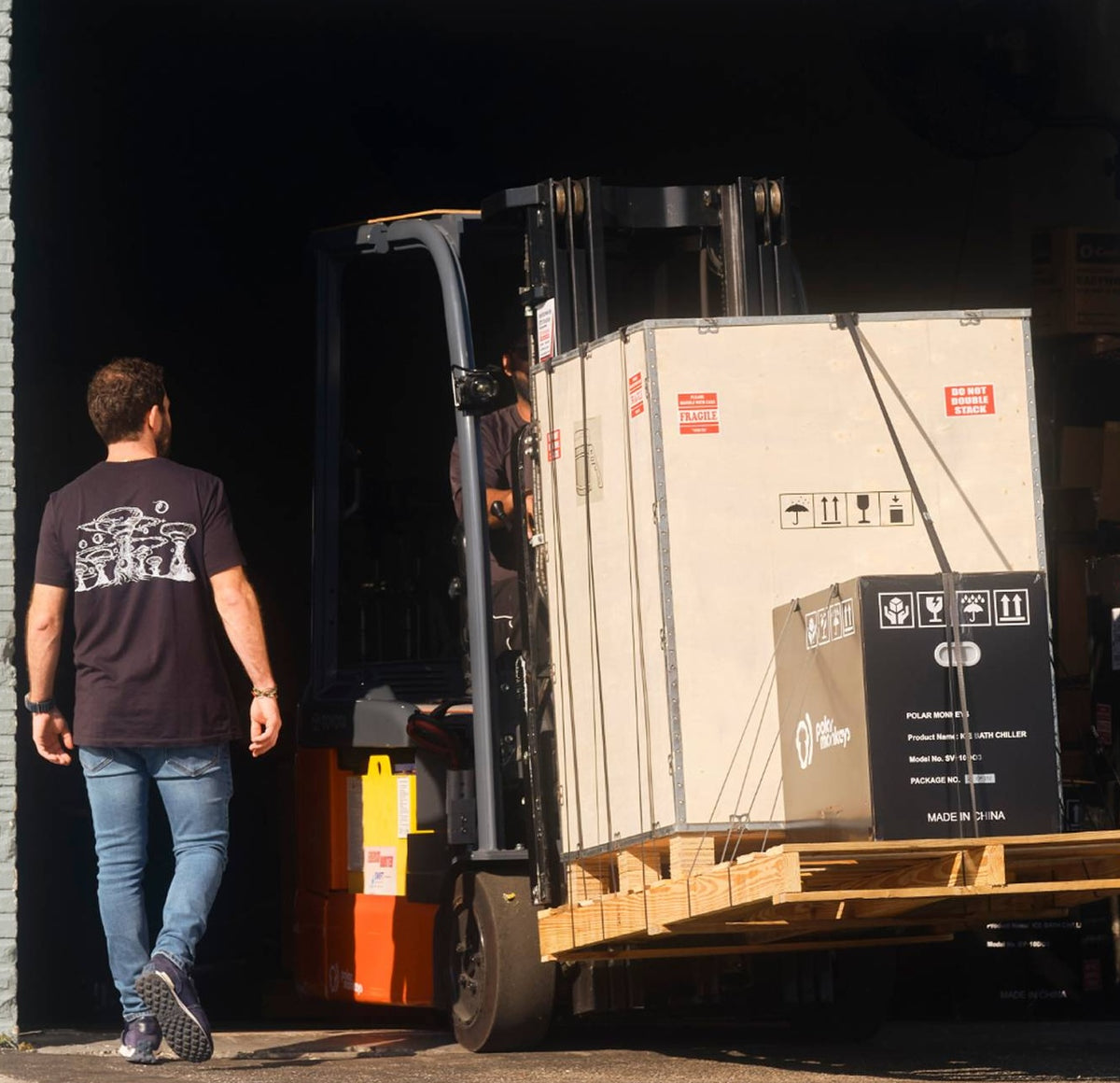 A technician providing White-glove Installation guides a forklift as it delivers large crates on a wooden pallet into a dimly lit warehouse.