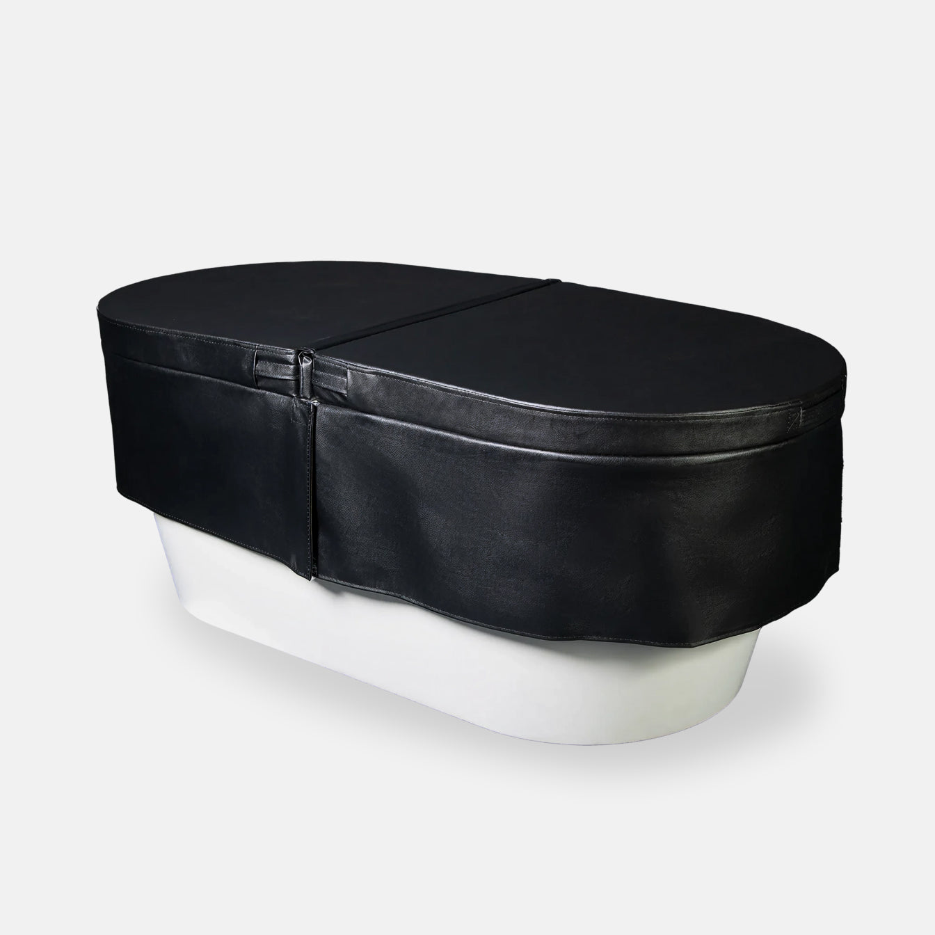 An Insulated Cold Plunge Cover in black, crafted from marine-grade synthetic leather with a zipper and fitted design, covers a white oval tub set against a plain light gray background.