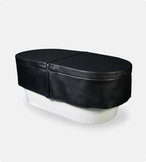 An Insulated Cold Plunge Cover in black, crafted from marine-grade synthetic leather with a zipper and fitted design, covers a white oval tub set against a plain light gray background.