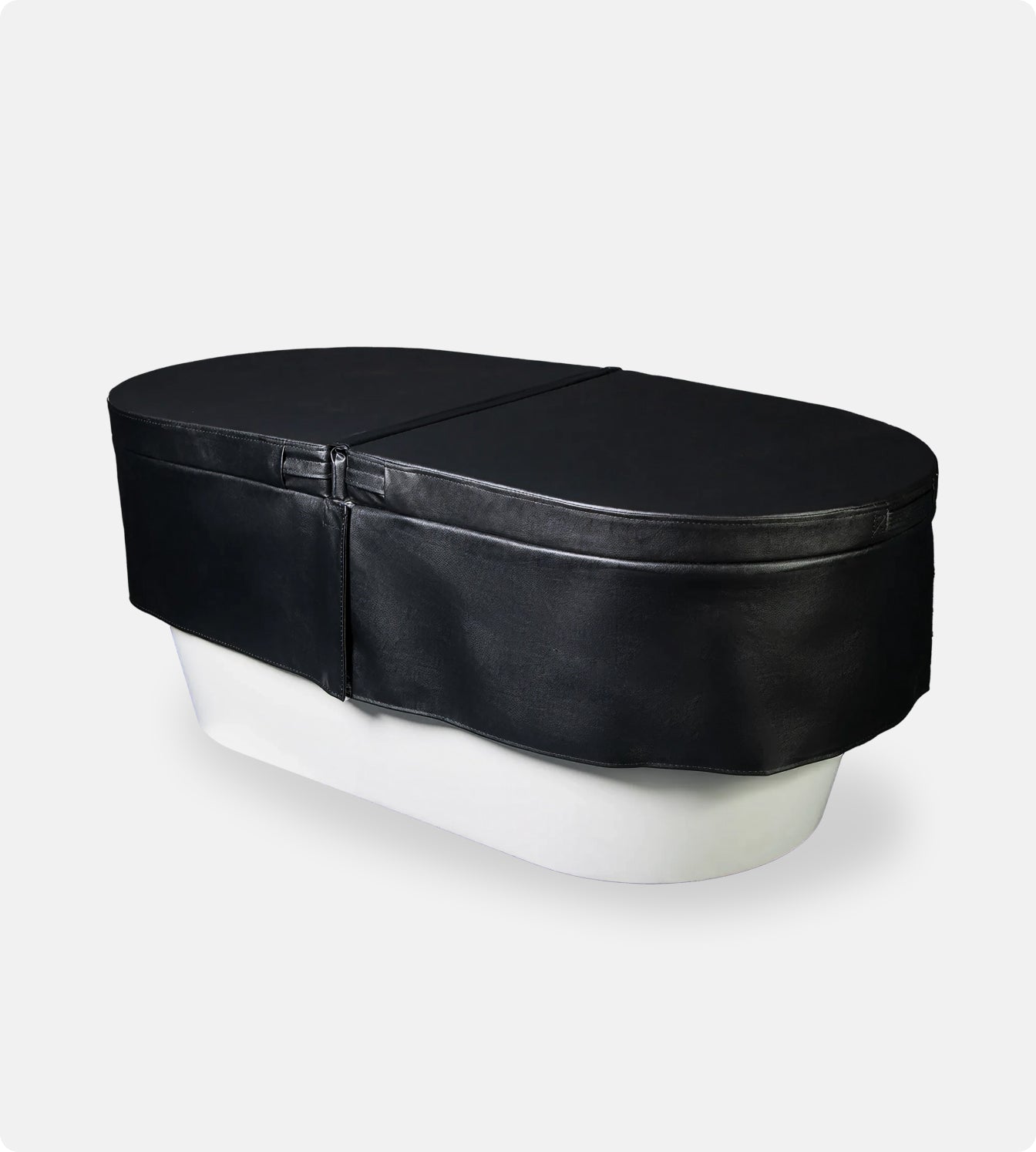 An Insulated Cold Plunge Cover in black, crafted from marine-grade synthetic leather with a zipper and fitted design, covers a white oval tub set against a plain light gray background.