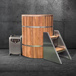 The Star Treatment 2.0, a tall, round wooden cold plunge tub with metal bands, stands on stone flooring—ideal for premium or compact spaces. Beside it are a metal-wood step ladder and a compact wheeled chiller against a dark wall.